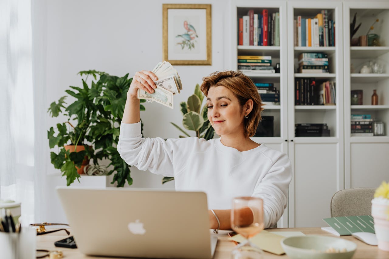 woman-sitting-in-an-office-in-front-of-a-laptop-and-waving-cash After-selling -digital-property.