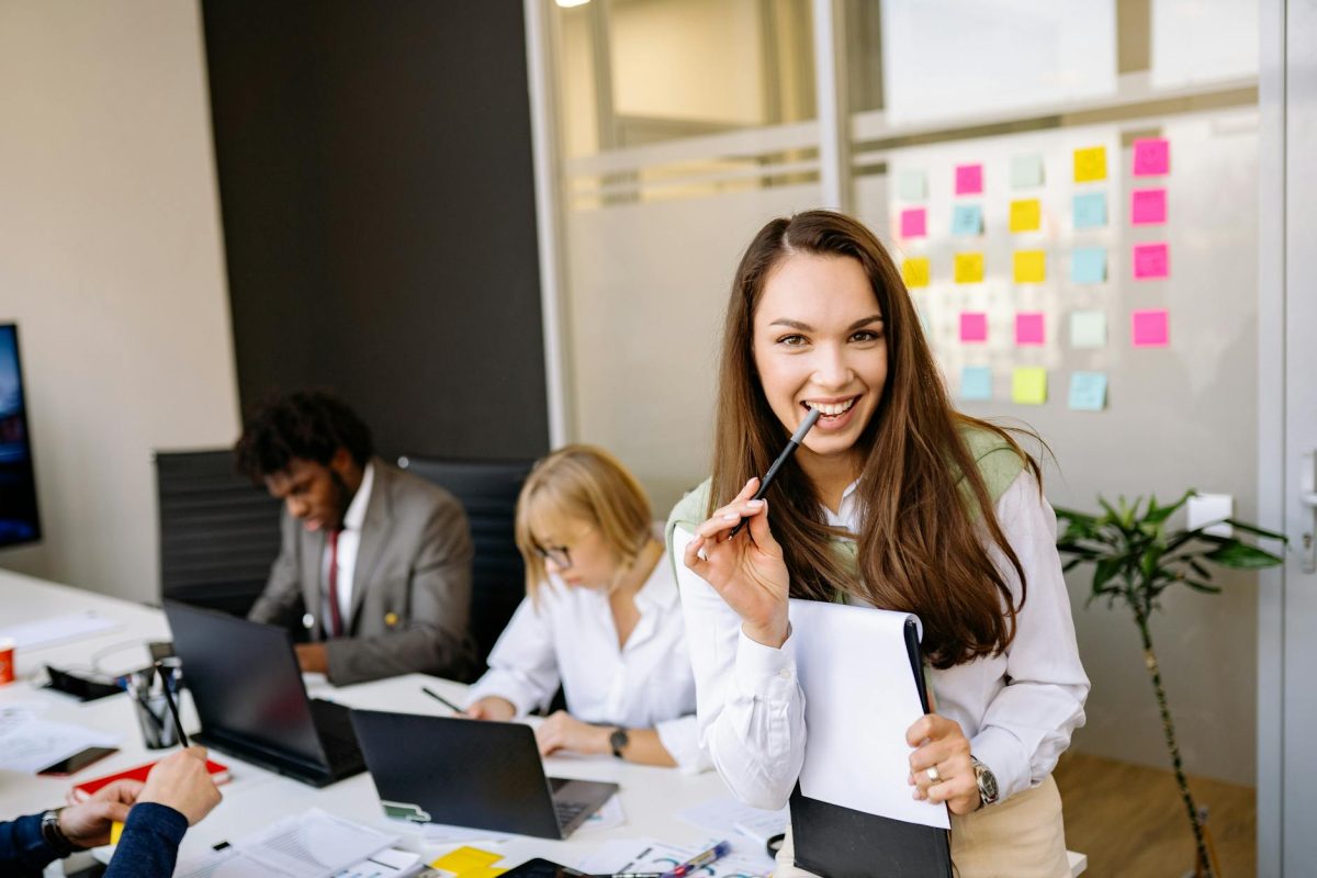 A woman the owner of an AI company standing in an office holing pen by her mouth.